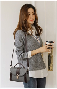 Detail of grey textured crossbody bag with brown leather strap and gold metal buckle