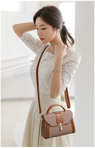 Detail of taupe woven crossbody bag with brown leather accents and gold metal lock on a model