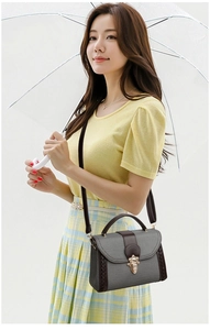 Detail of grey textured crossbody bag with brown leather trim and vintage gold buckle