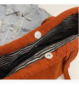 Detail of magnetic buckle and striped lining inside a caramel corduroy tote bag