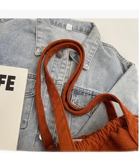Detail of orange corduroy tote bag strap on denim jacket showing fabric texture