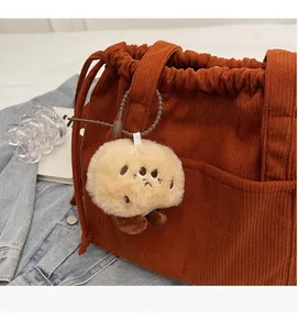 Detail of cute beige plush charm attached to a brown corduroy tote bag strap