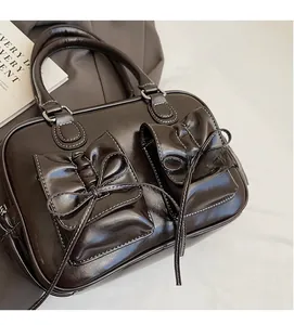 Detailed view of dark brown glossy leather handbag with two bow-adorned front pockets
