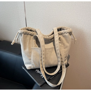 Detail of beige corduroy tote bag showing the drawstring closure and front pocket feature