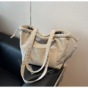 Detail of off-white corduroy tote bag showing drawstring closure and front pocket texture