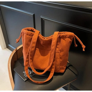Detail of orange corduroy tote bag with drawstring closure and front pocket on black chair