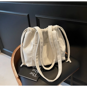 Close-up of cream corduroy tote bag with drawstring closure and front pocket on chair