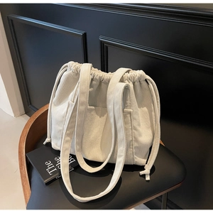 Detail of white corduroy tote bag showing the drawstring closure and outer pocket texture