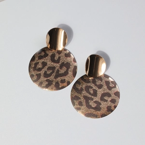 Detail of leopard print disc earrings with gold metal studs on a light grey background