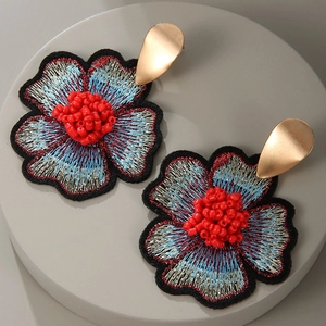 Detailed macro of handmade flower earrings with blue embroidery and red bead center