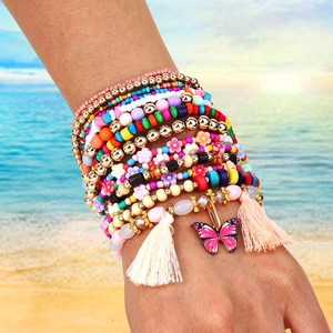 Dettaglio di bracciali con perline colorate, farfalla e nappa indossati su un polso