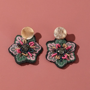 Détail de boucles d'oreilles brodées de fleurs avec perles et clous dorés