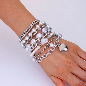 Détail d'un bracelet multi-rangs avec perles et pendentif cœur argenté porté au poignet