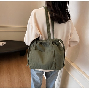 Detail of green corduroy tote bag with drawstring closure and large front pocket on model