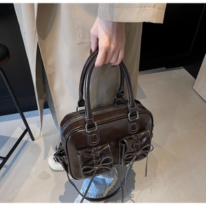 Detail of dark brown glossy patent leather handbag with bow accents and contrast stitching