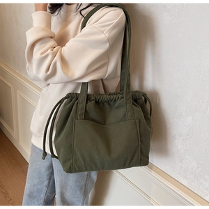Detail of green corduroy tote bag featuring drawstring closure and front pocket
