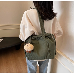 Detail of dark green corduroy tote bag featuring drawstring closure and plush pendant