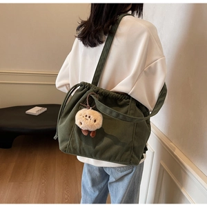 Detail view of dark green corduroy tote bag with drawstring and plush charm on model