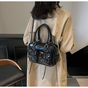 Detail of vintage black patent leather handbag with bow pockets on a beige trench coat