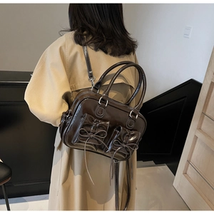 Detail of dark brown patent leather handbag with bow accents and contrast white stitching