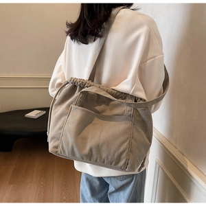 Detail of beige corduroy tote bag showing the drawstring closure and front pocket feature