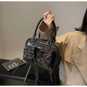 Detail of dark brown glossy patent leather handbag with bow drawstring pockets