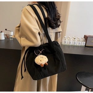Detail of black corduroy shoulder bag with drawstring closure and plush pendant
