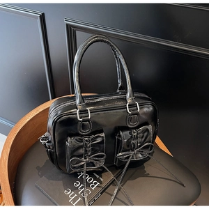 Detail of black patent leather handbag featuring bow-tie pockets and white stitching