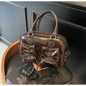 Detailed close-up of dark brown glossy patent leather handbag with bow pocket design