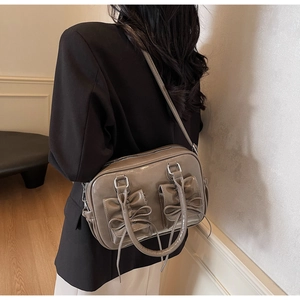 Macro detail of taupe high-gloss crossbody bag featuring dual decorative bow accents