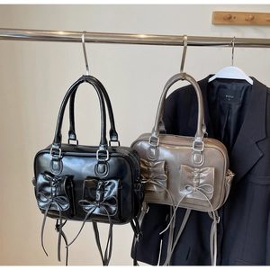 Detail of glossy leather handbags in black and taupe with unique bow-decorated front pockets
