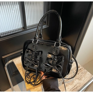 Detail of black glossy handbag featuring bow pockets and contrast stitching accents