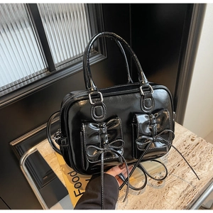 Detail of black glossy handbag with white contrast stitching and bow pocket accents