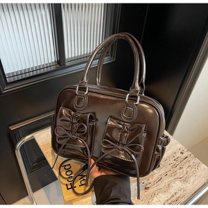 Macro detail of dark brown glossy patent leather handbag with bow pocket design