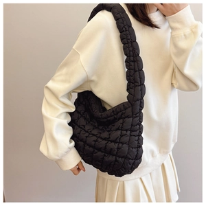 Detail of a black quilted cloud crossbody bag worn by a model in a casual outfit