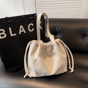 Minimalist beige corduroy tote bag with drawstring closure and large front pocket on sofa