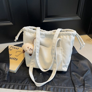 Beige corduroy tote bag with drawstring closure and teddy bear charm on wood background