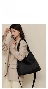 Fashionable black nylon tote bag with wide shoulder strap worn by a model in suit