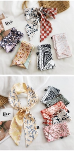 Détail d'un foulard en soie noué sur un sac en paille aux motifs floraux et géométriques