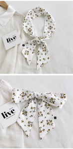Détail d'un foulard étroit à fleurs noué en boucle sur un fond en lin beige texturé