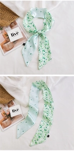 Vue détaillée d'un foulard étroit en soie vert clair avec motifs noué sur un sac en paille