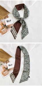 Détail d'un foulard étroit au toucher soie avec motifs marron foncé et fleurs vertes
