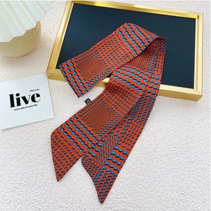Détail d'un foulard étroit orange et bleu avec motif géométrique sur un support doré