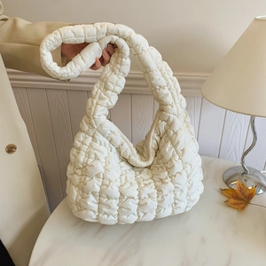 Quilted cloud crossbody bag with soft bubble texture on a white marble table