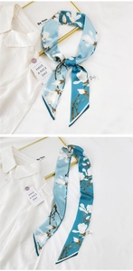 Detail of blue silk scarf with white magnolia print on a white shirt background