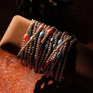 Detailed close-up of multi-layer gold beaded bracelets with colorful resin accents on a pillow