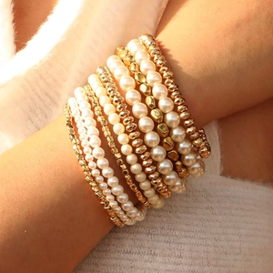 Close-up of stacked faux pearl and gold beaded bracelets on a model's wrist