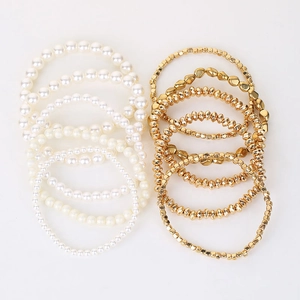 Detailed view of layered elastic bracelets with white faux pearls and gold beads