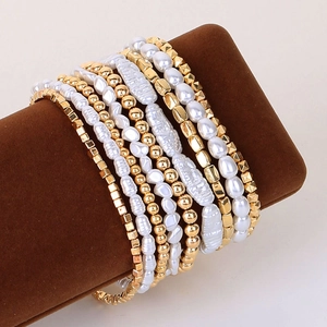 Detail of layered bracelet set featuring faux pearls and golden CCB beads on a brown stand