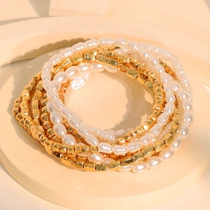 Stackable gold beaded bracelet set with oval faux pearls and geometric charms on a display stand